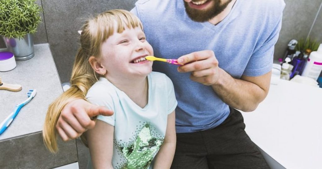 A father is helping his daughter brush her teeth to maintain oral hygiene