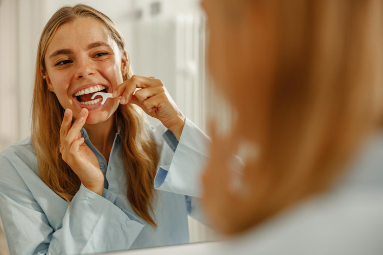 a woman in flossing her teeth in front of a mirror.