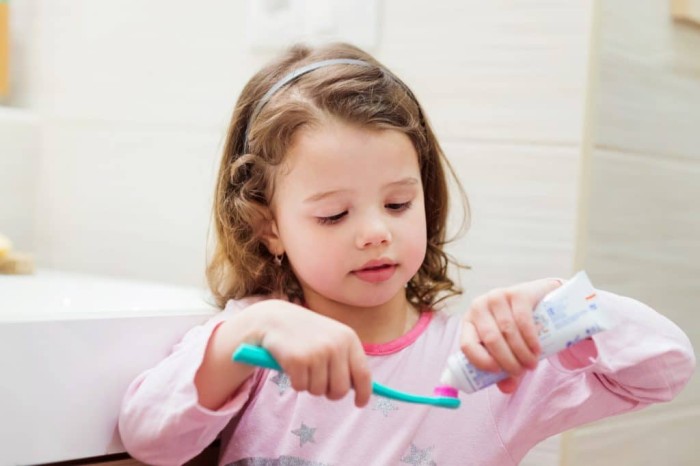 A little girl applying toothpaste to her toothbrush before brushing