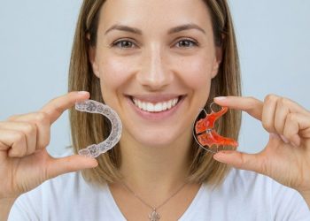 A smiling young woman holding two different types of retainers up to the camera.